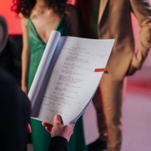 Actors in a studio review a script, preparing for a scene against a vibrant background.