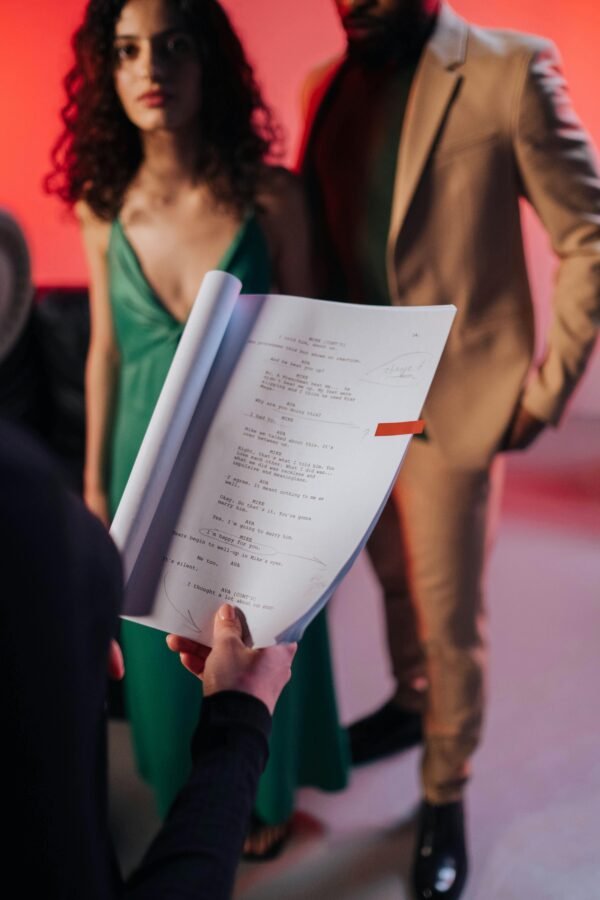Actors in a studio review a script, preparing for a scene against a vibrant background.